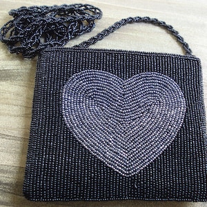 Puede incluir: Un bolso de noche negro de cuentas con un dise&ntilde;o de coraz&oacute;n plateado. El bolso tiene una correa de cadena.