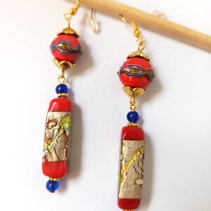 May include: A pair of long dangle earrings with red and gold glass beads. The top bead is round and the bottom bead is rectangular. The beads are separated by blue glass beads.