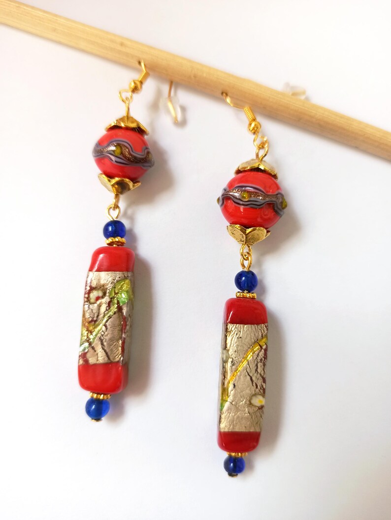 May include: A pair of long dangle earrings with red and gold glass beads. The top bead is round and the bottom bead is rectangular. The beads are separated by blue glass beads.
