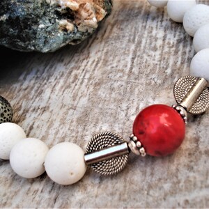 May include: White lava rock beads with silver spacers and a red gemstone bead. The bracelet has a simple, elegant design.