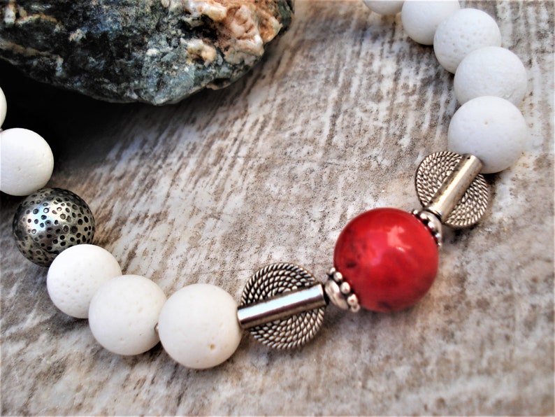May include: White lava rock beads with silver spacers and a red gemstone bead. The bracelet has a simple, elegant design.