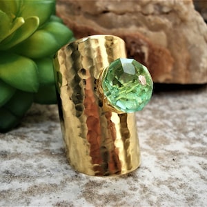 Puede incluir: Un anillo de banda martillado de oro con una gran piedra preciosa verde facetada.