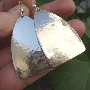 May include: A pair of silver hammered earrings with a curved, teardrop shape. The earrings have a textured, hammered finish.