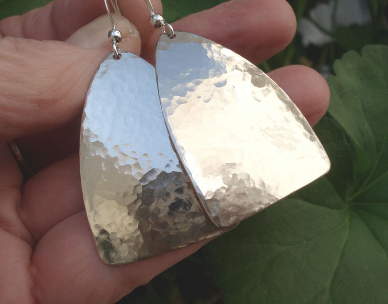 May include: A pair of silver hammered earrings with a curved, teardrop shape. The earrings have a textured, hammered finish.