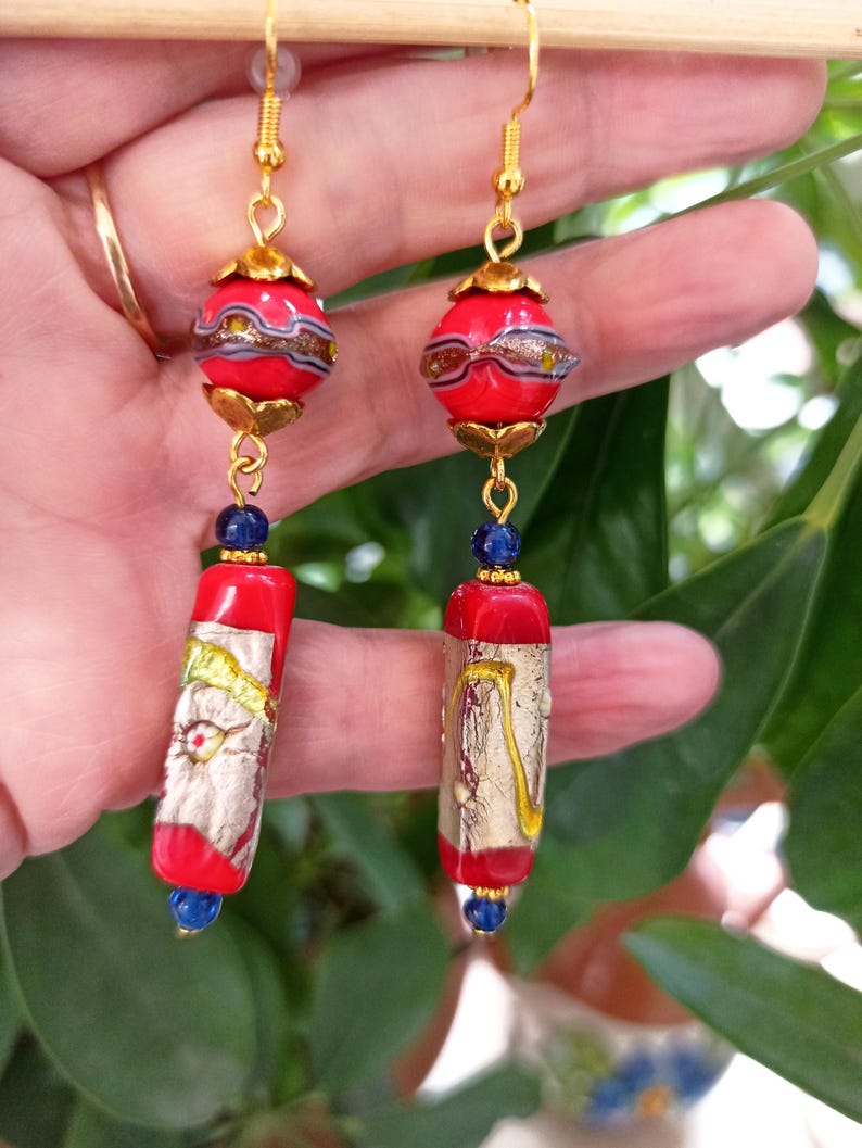 May include: Red and gold glass bead earrings with blue accents. The earrings feature a round bead with gold accents and a rectangular bead with gold leaf accents.