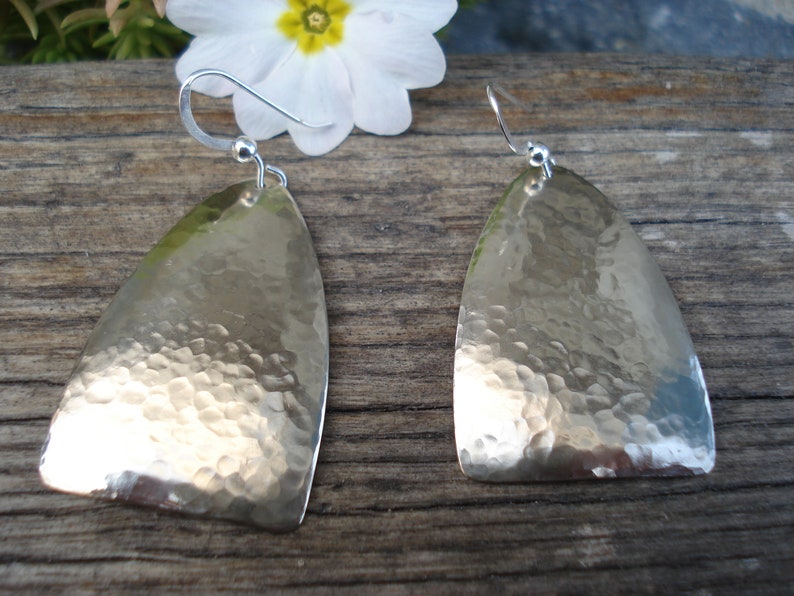 May include: A pair of silver earrings with a hammered texture. The earrings are shaped like a teardrop and have a hook fastening.