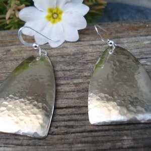 May include: A pair of silver earrings with a hammered finish. The earrings are shaped like a teardrop and have a simple hook fastening.