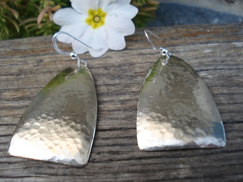 May include: A pair of silver earrings with a hammered finish. The earrings are shaped like a teardrop and have a simple hook fastening.