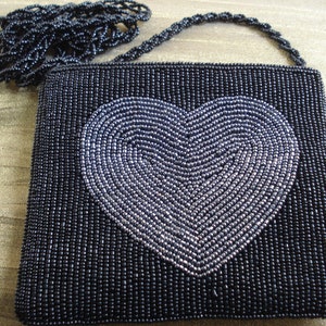 Puede incluir: Un bolso de noche negro de cuentas con un dise&ntilde;o de coraz&oacute;n plateado. El bolso tiene una correa de cadena de cuentas.