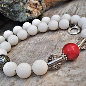 May include: A white lava rock beaded necklace with a red coral bead and silver accents.