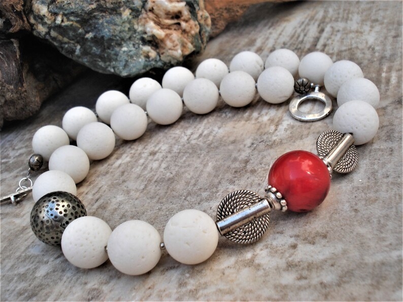 May include: A white lava rock beaded necklace with a red coral bead and silver accents.