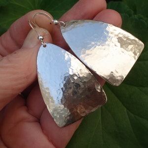 May include: A pair of silver hammered dangle earrings with a teardrop shape. The earrings are made of metal and have a shiny finish.