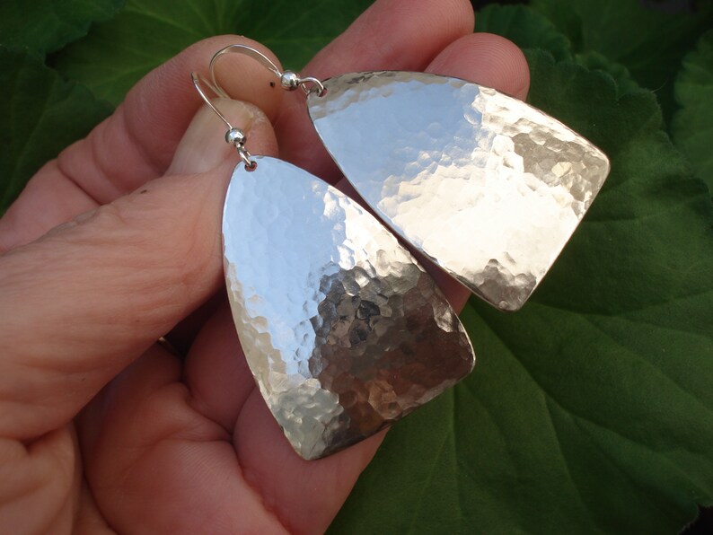 May include: A pair of silver hammered dangle earrings with a teardrop shape. The earrings are made of metal and have a shiny finish.