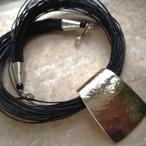 May include: A long black cord necklace with a large, hammered silver pendant.