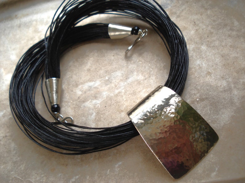 May include: A long black cord necklace with a large, hammered silver pendant.