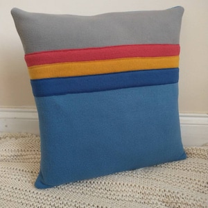 May include: A blue, yellow, red and grey striped cushion with a soft, fluffy texture.