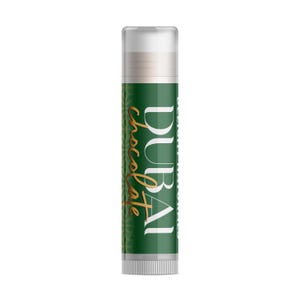 May include: A lip balm tube with a white cap and a green label. The label features the word "DUBAI" in white and "Chocolate" in gold script. The tube is cylindrical and appears to be a cosmetic product.