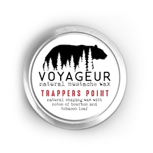 Op de afbeelding: Een zilveren blik met een zwart-wit etiket. Het etiket toont een zwart beren silhouet in een bosomgeving. De tekst op het etiket luidt "VOYAGEUR natuurlijke snorwax TRAPPERS POINT natuurlijke vormgevende wax met tonen van bourbon en tabaksblad."