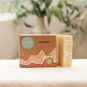 May include: A bar of natural soap in a cardboard box with a mountain landscape design. The box is labeled "Patchouli" and "Bona Fide".