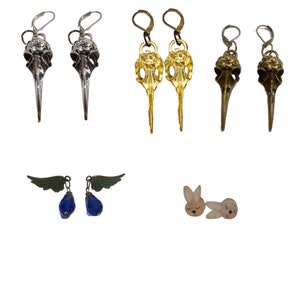 Könnte beinhalten: Sortiment an Ohrringen mit verschiedenen Designs, darunter Vogelschädel, Flügel und Kaninchen. Die Ohrringe sind aus Metall und haben verschiedene Oberflächen, darunter Gold, Silber und Blau.