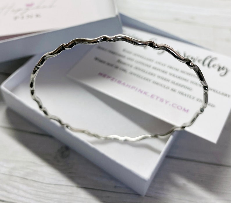 May include: A silver bangle bracelet with a wavy, textured design. The bracelet is in a white box with a card that says "#elizabethpink.etsy.com".
