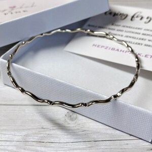 May include: A silver bangle bracelet with a wavy design. The bracelet is in a white box with a card that says "Caring for your jewelry".