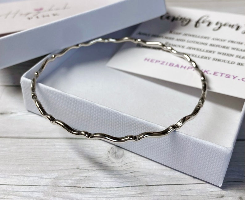 May include: A silver bangle bracelet with a wavy design. The bracelet is in a white box with a card that says "Caring for your jewelry".