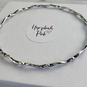 May include: A silver bangle bracelet with a wavy design. The bracelet is on a white background.