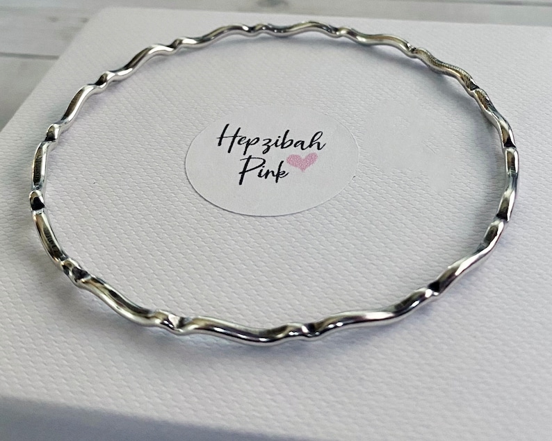 May include: A silver bangle bracelet with a wavy design. The bracelet is on a white background.