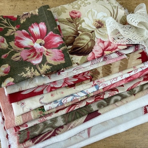 Può includere: Una pila di quadrati di tessuto piegati con vari motivi floreali e botanici in tonalità di rosso, rosa, verde e crema. La collezione include un pezzo di bordo in pizzo bianco drappeggiato sopra, con bordi grezzi visibili.