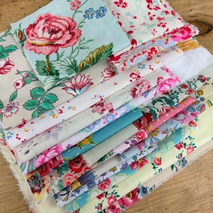 Könnte beinhalten: Ein Stapel quadratischer Stoffstücke mit verschiedenen Blumenmustern in Rosa-, Rot-, Grün-, Blau- und Gelbtönen auf weißem, cremefarbenem und hellblauem Hintergrund. Die Stoffstücke haben ausgefranste Kanten und liegen übereinander.