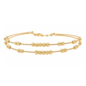 May include: A double-strand gold bracelet featuring thin, twisted cable chains. The bracelet is adorned with small, round, textured gold beads spaced along both strands, secured with a gold lobster claw clasp at the back.