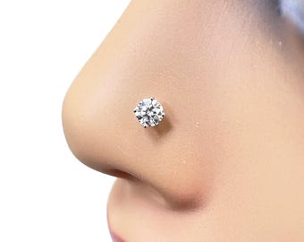 May include: A clear, round-cut cubic zirconia nose stud. The stud is set in a silver-colored metal and is shown on a person's nose. The stud is a small, sparkly accessory.