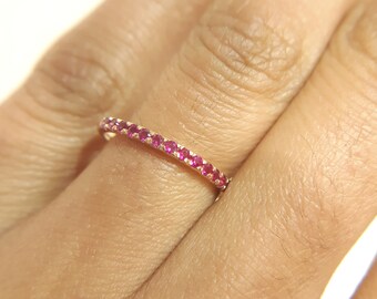 Puede incluir: Un fino anillo de banda de oro con una fila de pequeñas piedras de rubí rojo brillante.