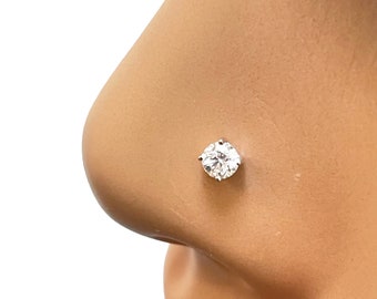 May include: A clear round gemstone nose ring with a silver setting. The ring is worn in a person's left nostril.