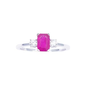 Peut inclure: Bague en argent ornée d'une pierre centrale magenta rectangulaire, flanquée de deux pierres claires rondes plus petites. Le design de la bague est mis en valeur sur fond blanc, soulignant l'éclat des pierres.