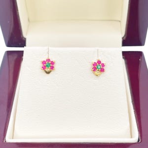 May include: A pair of gold flower-shaped stud earrings with pink and green gemstones. The earrings are displayed in a burgundy velvet jewelry box.
