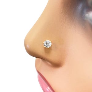 May include: A gold nose ring with a clear round gemstone.