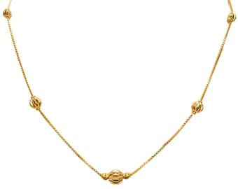 Op de afbeelding: Een delicate gouden ketting met een fijne ketting en zes getextureerde, bolvormige kralen. De kralen hebben een geribbeld patroon en zijn gelijkmatig verdeeld. De ketting staat tegen een effen witte achtergrond.