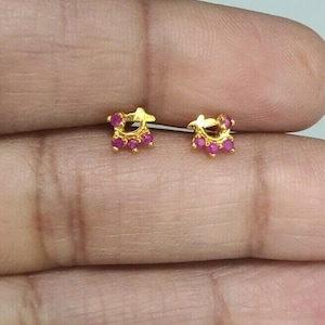 Op de afbeelding: Een paar kleine gouden oorbellen, elk met een stervormig ontwerp en een cluster van kleine, ronde, roze edelstenen. De oorbellen worden getoond tegen een neutrale achtergrond.