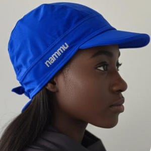 May include: A bright blue swim cap with a stiff brim and a tie-back closure. The word nammu is printed in white lettering on the side of the cap. The cap is constructed from a smooth, flexible material designed to fit securely around the head.