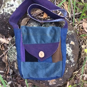 May include: A blue, purple, brown, and black patchwork crossbody bag with a wooden button. The bag has a long strap and a flap closure.