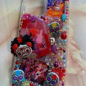 Puede incluir: Una funda transparente para tel&eacute;fono decorada con cuentas de colores, purpurina y abalorios. La funda presenta una imagen de los personajes de la pel&iacute;cula "Coco" y varios abalorios de calavera de az&uacute;car.