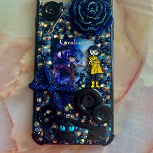 Puede incluir: Carcasa negra para iPhone con una rosa azul y negra, un gato negro, botones y una imagen de Coraline de la pel&iacute;cula Coraline.