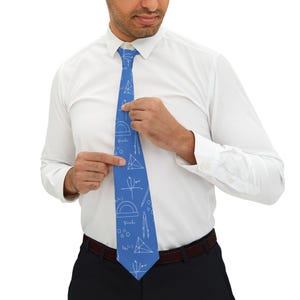 Puede incluir: Una corbata azul con un patrón repetitivo de líneas blancas que muestra símbolos matemáticos, formas geométricas, transportadores, compases y ecuaciones algebraicas, sobre una camisa blanca y pantalones oscuros.
