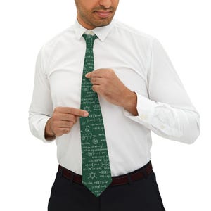 Peut inclure: Une cravate vert foncé ornée d'un motif répétitif blanc composé de diverses formules scientifiques et mathématiques, de structures chimiques et d'équations. La cravate est portée avec une chemise blanche à manches longues et un pantalon sombre.