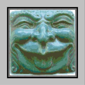Könnte beinhalten: Nahaufnahme einer grünen Steinskulptur eines Gesichts mit einem breiten, zahnigen Grinsen. Die Skulptur ist detailliert mit Falten um die Augen und den Mund, was ihr einen schelmischen Ausdruck verleiht.
