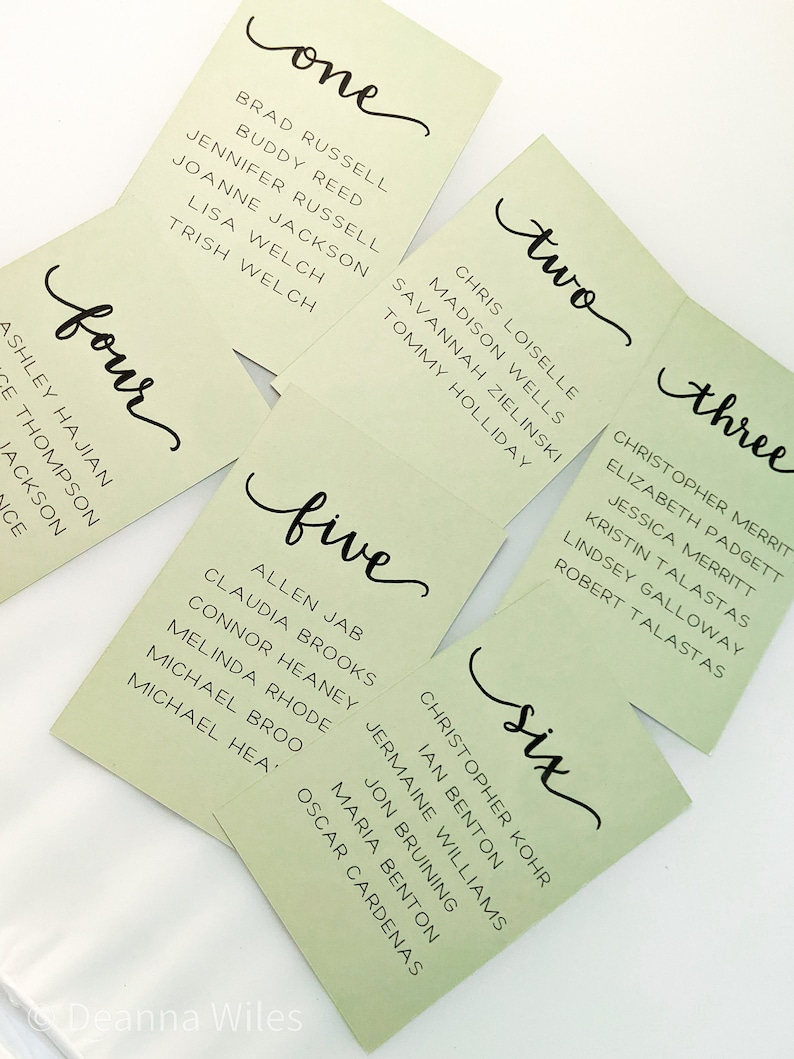 May include: Six green place cards with black calligraphy for a wedding or event. The cards are numbered one through six and list names for each number.