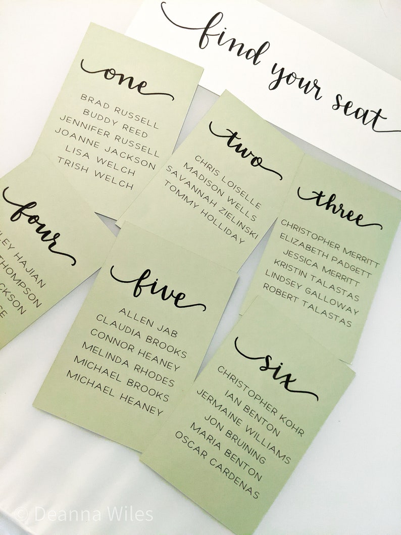 May include: Six green cards with black calligraphy, each with a number from one to six and a list of names. The cards are arranged in a semi-circle with the text "find your seat" at the top.