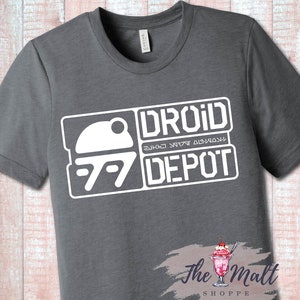 May include: Gray t-shirt with a white graphic design of a droid head and the text "DROID DEPOT" with a stylized font.